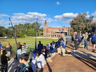 A lively sports event with students competing on the campus field under sunny skies.