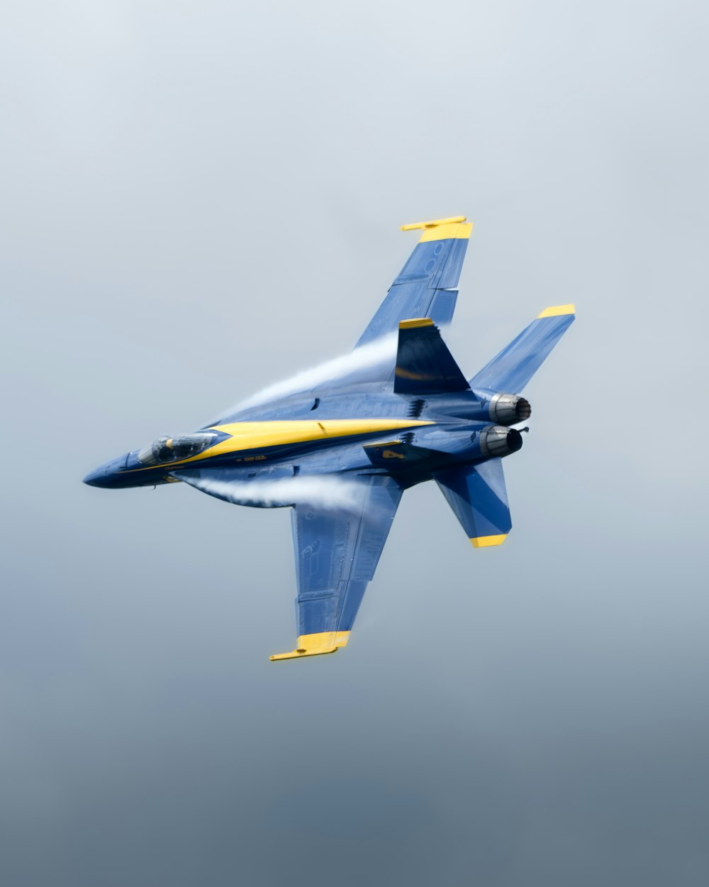 a blue and yellow fighter jet flying through a cloudy sky