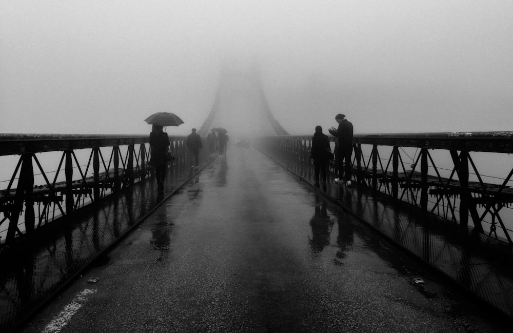 a group of people walking across a bridge in the rain