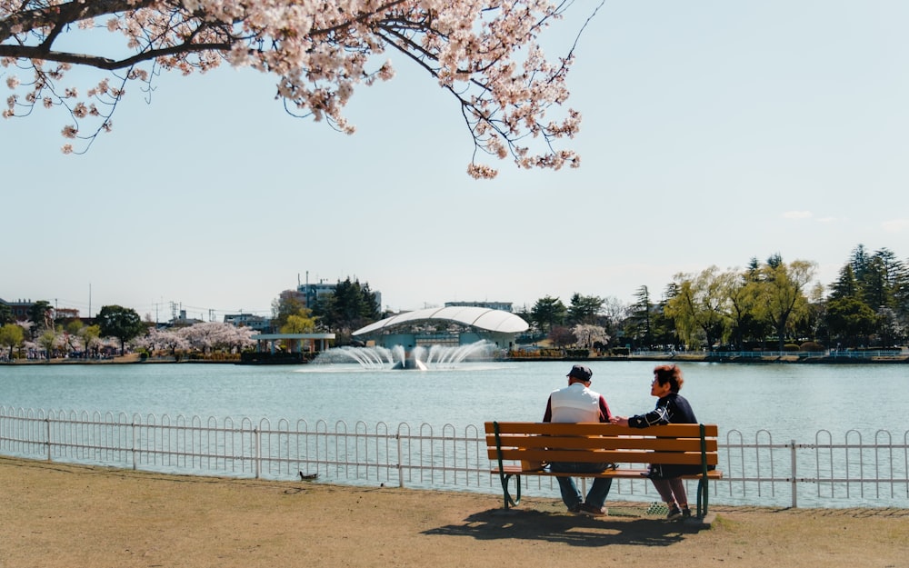 two people sitting on a bench near a lake