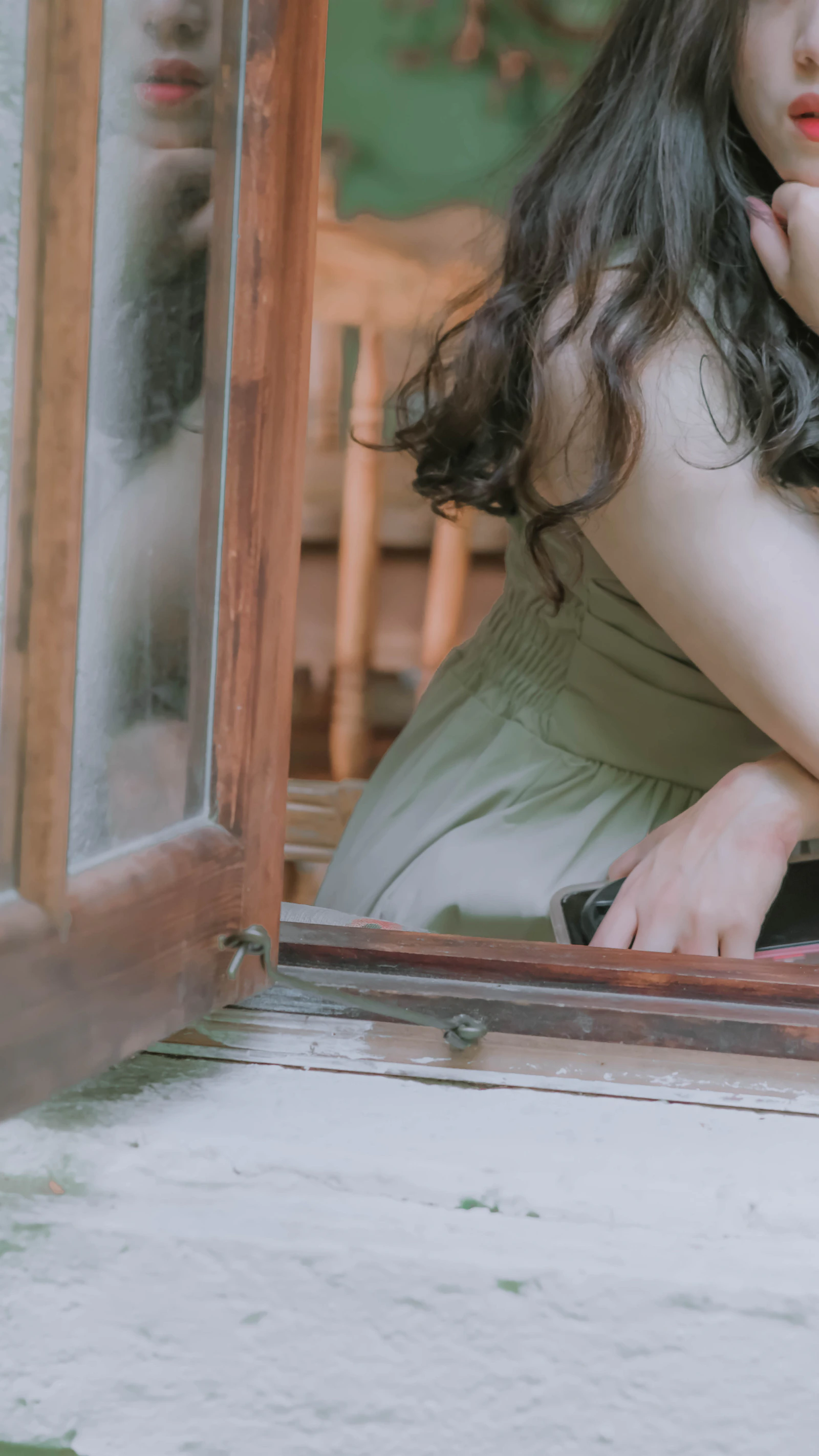 A woman sitting on a window sill in contemplation, hand resting against her chin