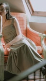 Model seated by a large window, dressed in soft pastel tones, embodying quiet luxury.