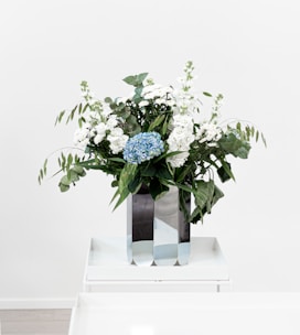 A bright bouquet of mixed seasonal flowers arranged in a minimalist white vase.