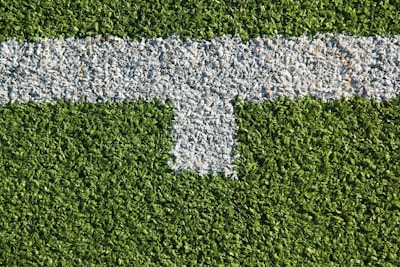 A patch of artificial grass with a thick white line running horizontally across it, intersected by a shorter vertical white line.