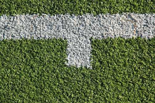 A patch of artificial grass with a thick white line running horizontally across it, intersected by a shorter vertical white line.
