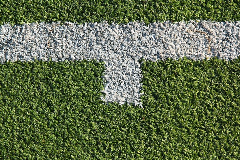 A patch of artificial grass with a thick white line running horizontally across it, intersected by a shorter vertical white line.