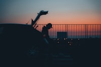 A man standing next to a car with the sun setting in the background