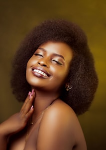 A close-up of a joyful woman gently touching her glowing, radiant skin in soft natural light.