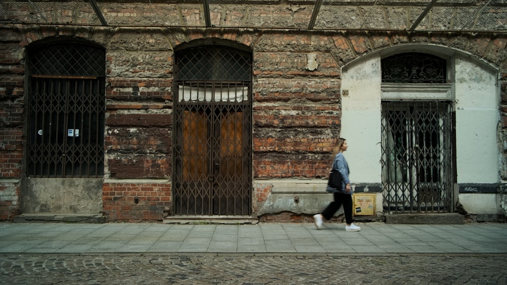 a woman walking down a street past a brick building
