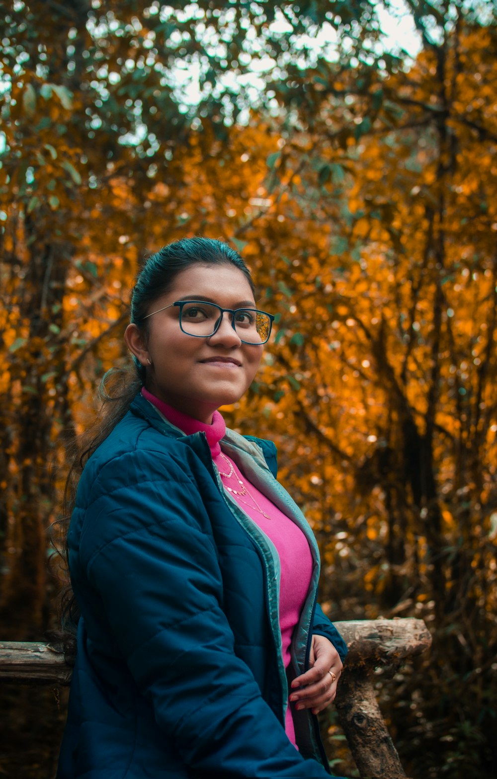 a woman wearing glasses standing in front of a forest