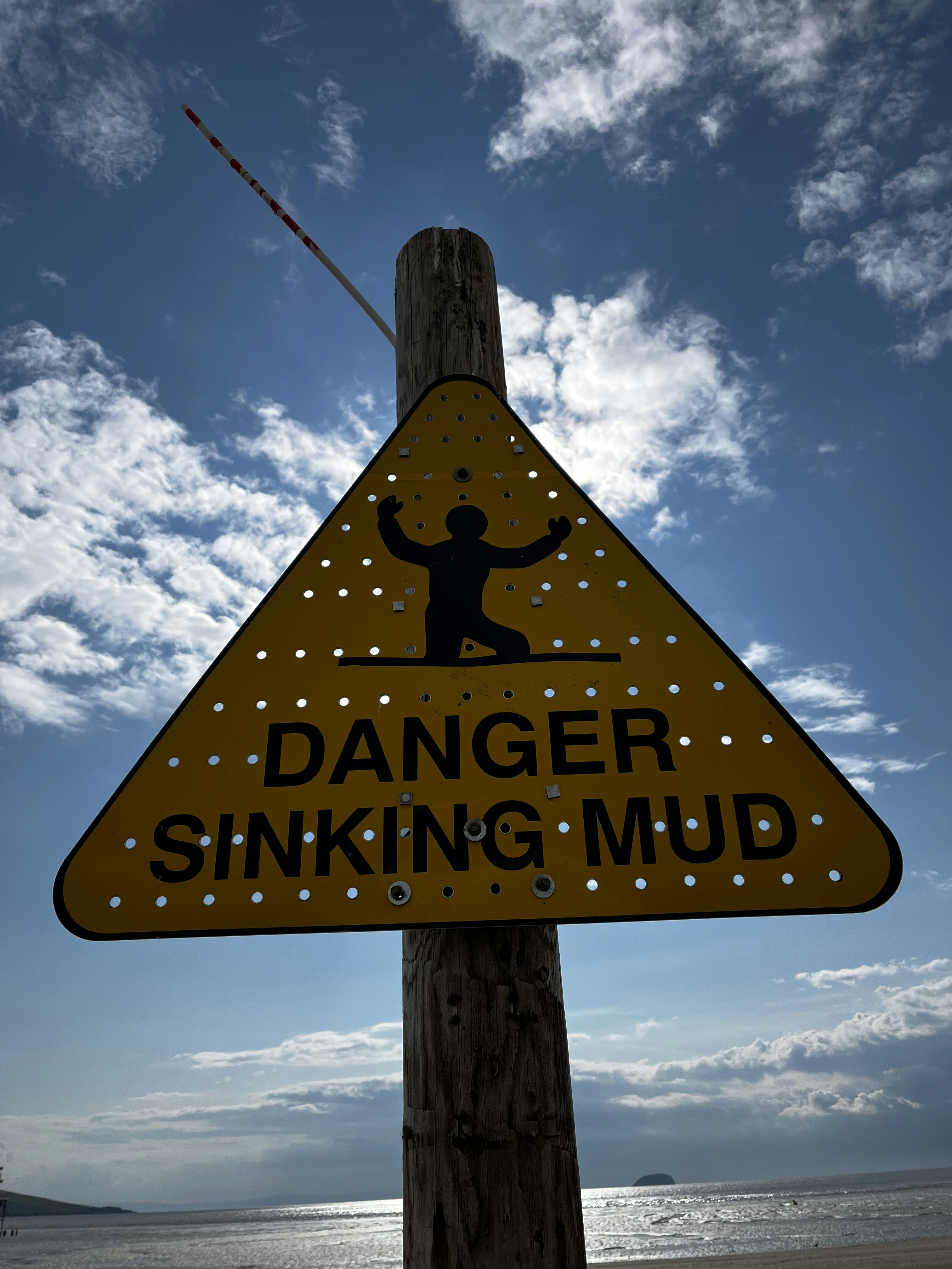 a warning sign on a wooden pole on a beach