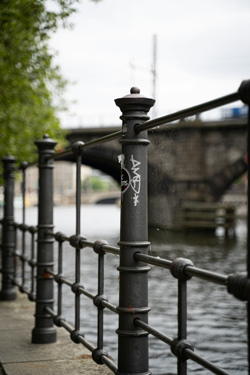 a black fence with graffiti on it next to a body of water