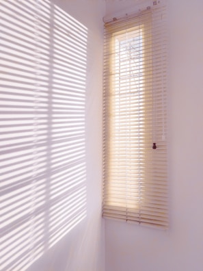 Cozy bedroom with minimalist decor and warm-toned window blinds casting gentle patterns.