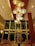 An elegant hotel lobby features a large, modern chandelier with multiple warm-colored, circular lights hanging from a high wooden ceiling. Below, there is a beautifully arranged centerpiece with tall glass vases filled with various flowers, including yellow, white, and orange blossoms. Comfortable seating is arranged throughout the lobby, and large windows provide a view to the outside.