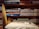 Several neatly folded fabrics in different patterns and colors are arranged on wooden shelves. Below the fabrics, there is a table with a few sewing items including a pair of scissors, a measuring tape, and a spool of thread. The shelves also have some boxes with labels. The setting gives a rustic and cozy feel.