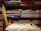 Several neatly folded fabrics in different patterns and colors are arranged on wooden shelves. Below the fabrics, there is a table with a few sewing items including a pair of scissors, a measuring tape, and a spool of thread. The shelves also have some boxes with labels. The setting gives a rustic and cozy feel.