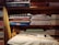 Several neatly folded fabrics in different patterns and colors are arranged on wooden shelves. Below the fabrics, there is a table with a few sewing items including a pair of scissors, a measuring tape, and a spool of thread. The shelves also have some boxes with labels. The setting gives a rustic and cozy feel.