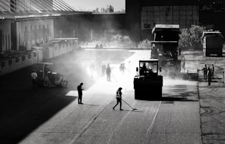 Workers smoothing asphalt on a large parking lot under a clear sky.