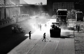 Wide shot of workers repairing a cracked road with asphalt layers under bright sunlight.