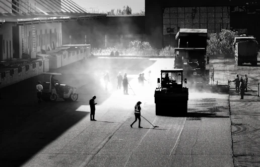 A team of workers applying thermoplastic road markings on a busy highway under bright daylight.