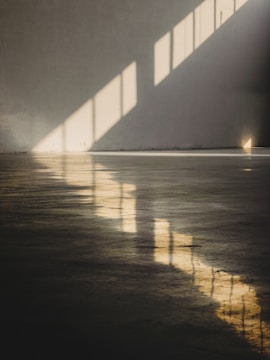 Sunlight filtering through minimalist window frames casting geometric shadows on a smooth concrete floor.