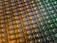 An array of intricate, patterned semiconductor chips with a reflective sheen, showing various colors and geometric patterns. The surface appears highly detailed with a grid-like structure.