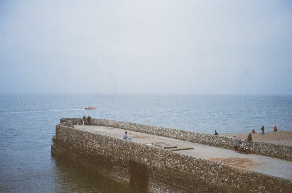 a group of people standing on top of a pier next to the ocean
