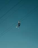 A person wearing a helmet and harness is zip lining across clear blue skies, suspended by cables.