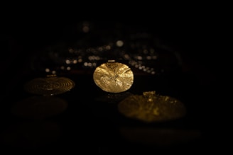 A close-up of intricately designed golden pendants with detailed patterns, illuminated against a dark background.