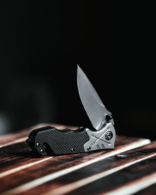 A sleek folding knife resting on a wooden table, highlighting its sharp blade and ergonomic handle.