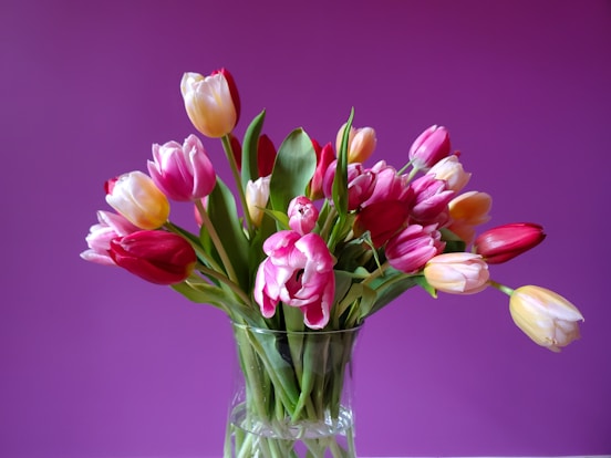 a vase filled with lots of pink and yellow tulips