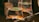 Two transparent plastic bags containing water and orange fish hanging from a metal rod. The background is slightly blurred with an object appearing to be a bucket or container.