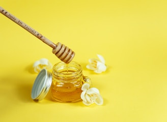 Close-up of a jar of golden honey with a wooden honey dipper dripping honey, surrounded by cerrado flowers.