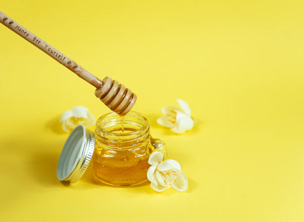 Close-up image of a jar filled with golden wildflower honey with a wooden honey dipper