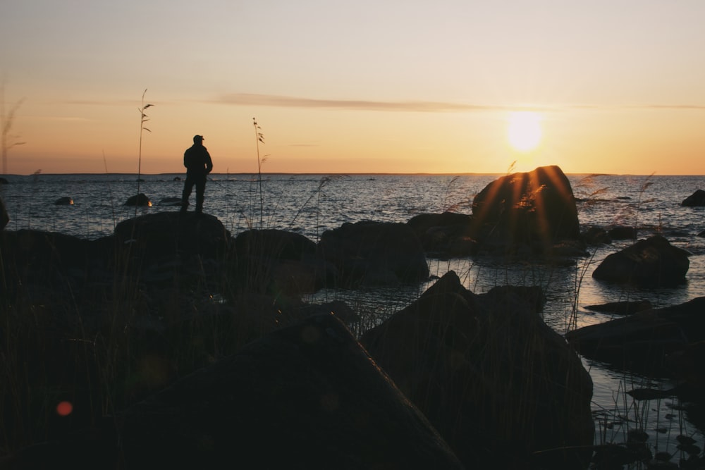 um homem em pé em uma rocha perto do oceano ao pôr do sol