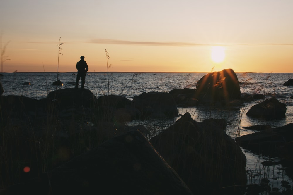 a man standing on a rock near the ocean at sunset