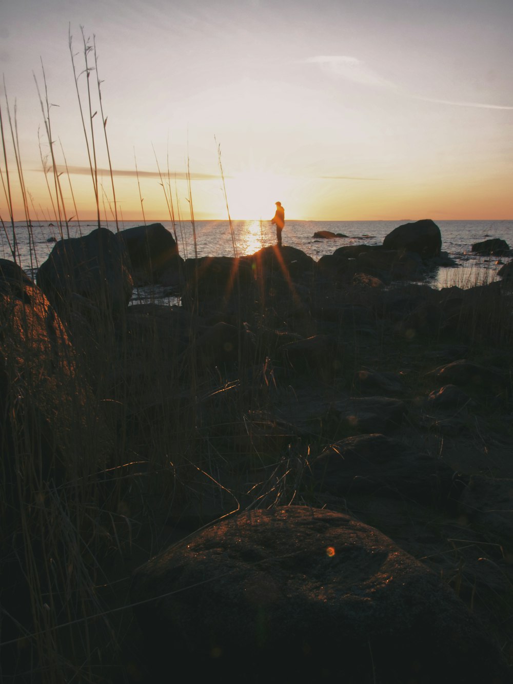 una persona in piedi su una spiaggia rocciosa al tramonto