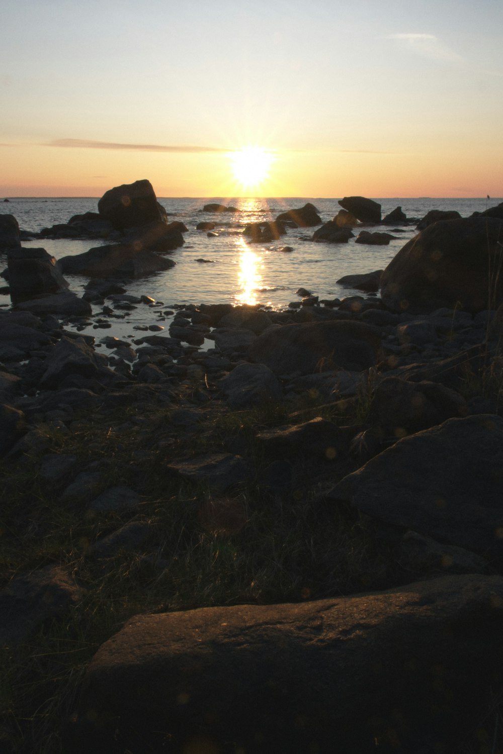 the sun is setting over the water and rocks