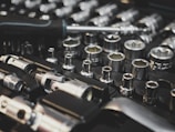 A collection of metal socket wrenches is neatly organized on a black foam tray, featuring various sizes and types. A screwdriver lies across the tools, hinting at readiness for work or repair.