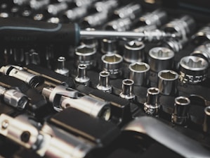 A collection of metal socket wrenches is neatly organized on a black foam tray, featuring various sizes and types. A screwdriver lies across the tools, hinting at readiness for work or repair.