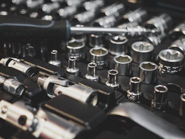 A collection of metal socket wrenches is neatly organized on a black foam tray, featuring various sizes and types. A screwdriver lies across the tools, hinting at readiness for work or repair.