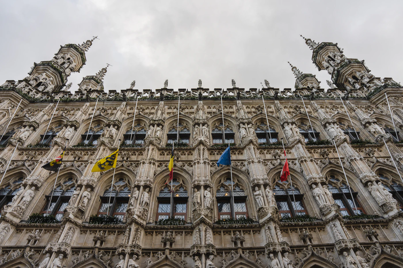 Готическая ратуша Лёвена на Grote Markt с каменной резьбой и флагами
