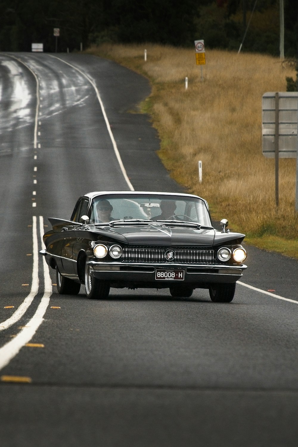 um carro preto dirigindo por uma estrada ao lado de um campo