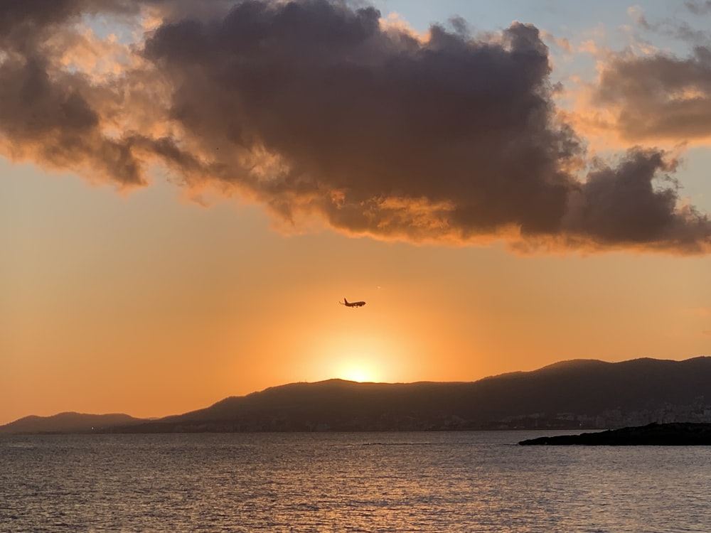 a plane flying over a body of water at sunset