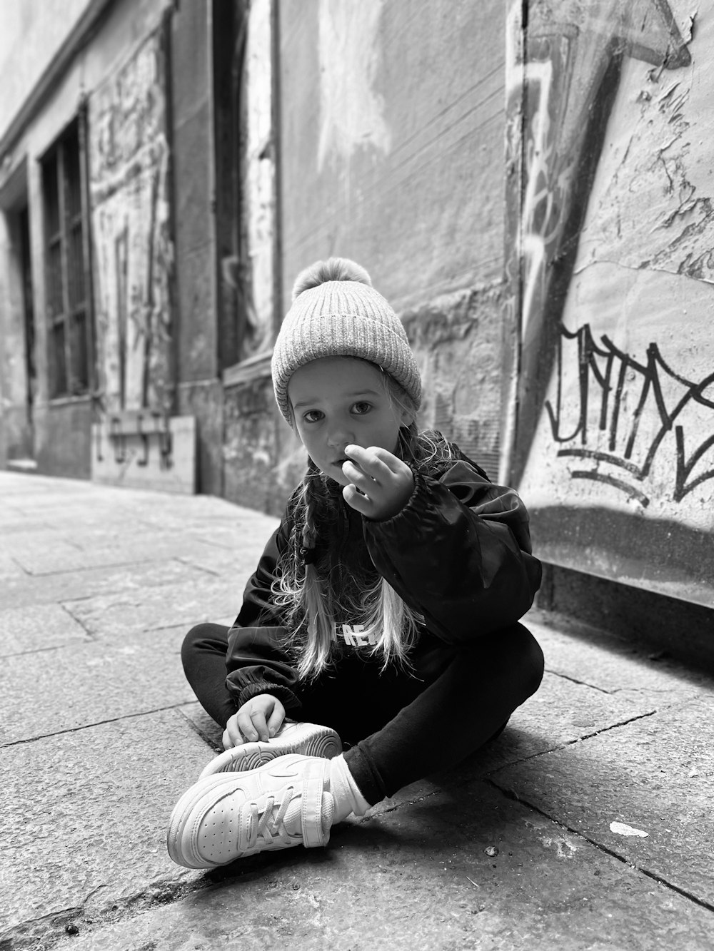a little girl sitting on the ground in front of a wall