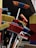 A variety of colorful brooms are clustered together, showcasing vibrant bristles in shades of red, blue, orange, and yellow. The brooms lean against an exterior wall, suggesting they are on display outside a store.