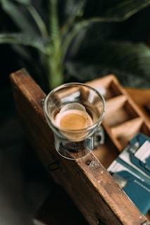 A steaming cup of espresso on a wooden table with a backdrop of vintage coffee sacks and green leaves.