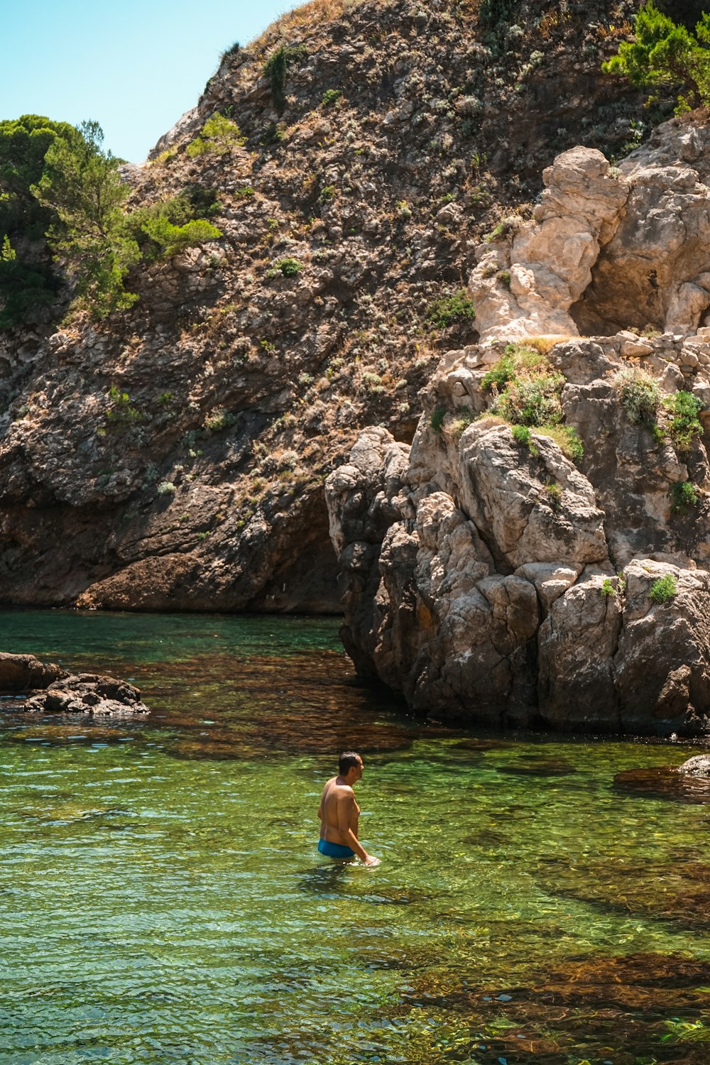 a man wading in the water near a rocky cliff