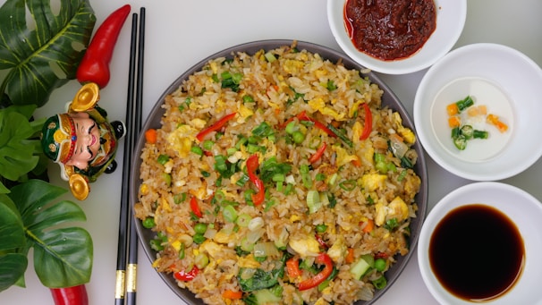 A vibrant dish of Chinese fried rice with colorful vegetables and chopsticks on a red and gold table setting.