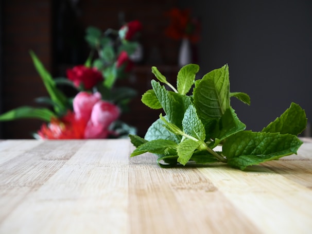 Freshly dried mint leaves in a rustic wooden bowl with a blurred background of a wellness drink.